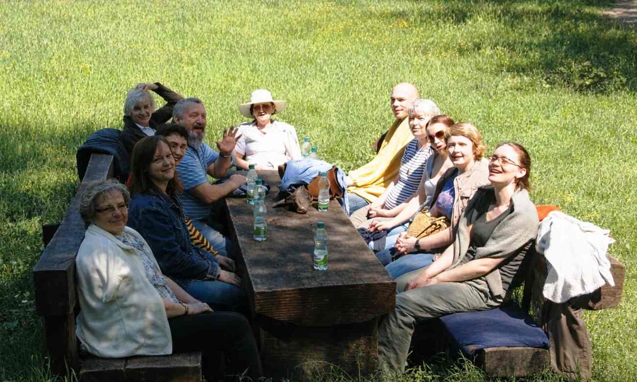 Skupina ľudí na drevenej lavici na lúke, s minerálkou položenou na stole